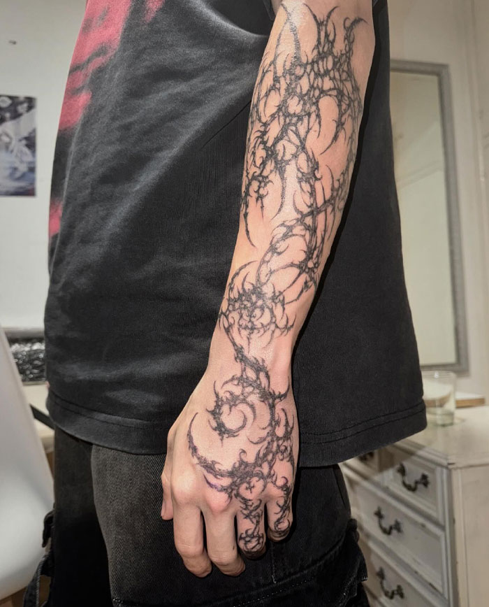 Arm with intricate cybersigilism tattoo, showcasing dark, swirling designs in a modern style.