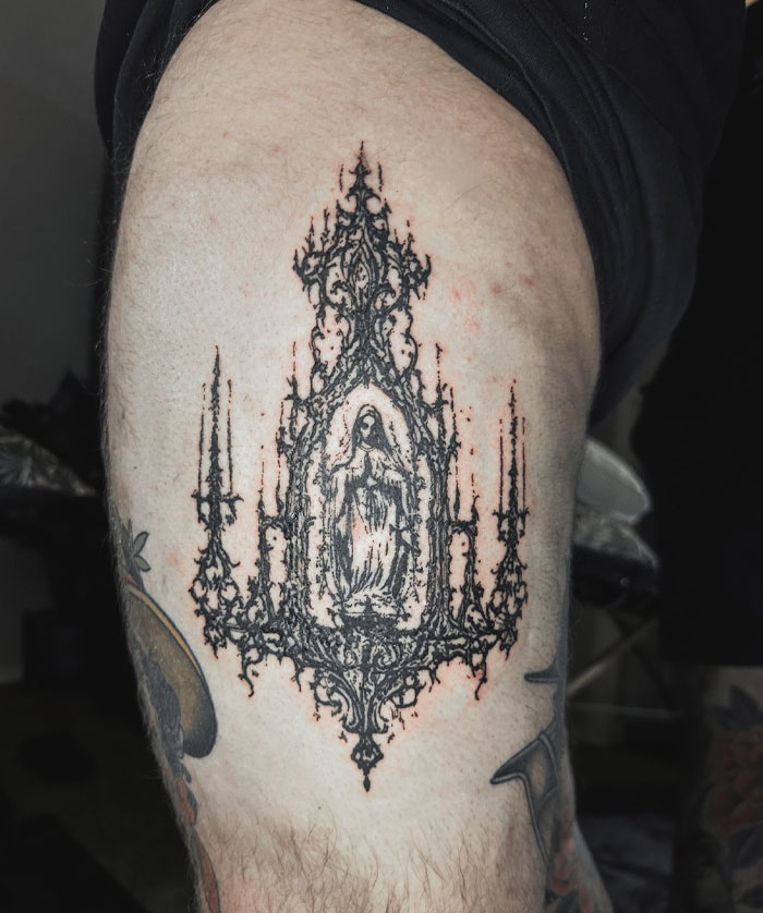 Ornate tattoo depicting religious symbolism in a detailed design on a person's leg, showcasing cybersigilism style.