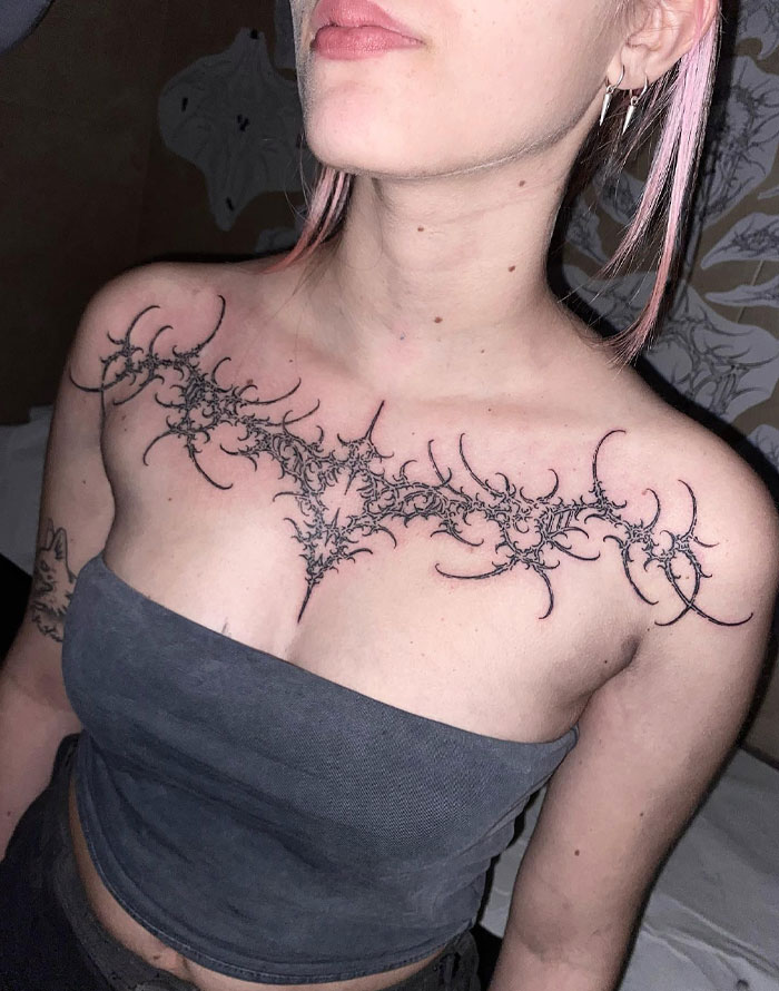 Woman with intricate black tattoo on chest reflecting cybersigilism style and symbolism.
