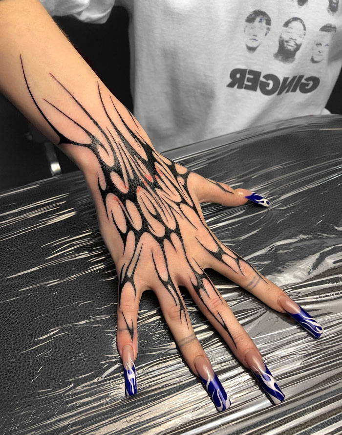 Hand with cybersigilism tattoo design and blue flame nails on a textured surface.
