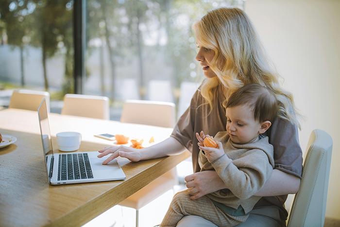 A mother multitasking with a laptop and her baby, highlighting family dynamics and childcare challenges.