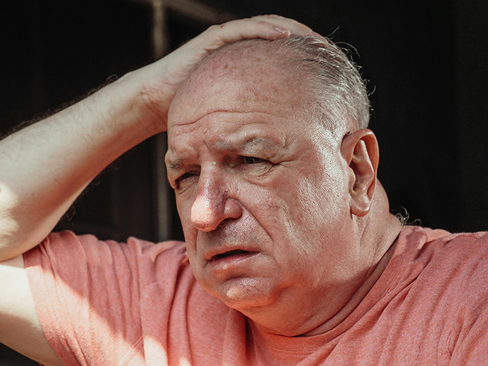 Elderly man in a pink shirt, looking upset and holding his head, related to babysitting incompetence topic.