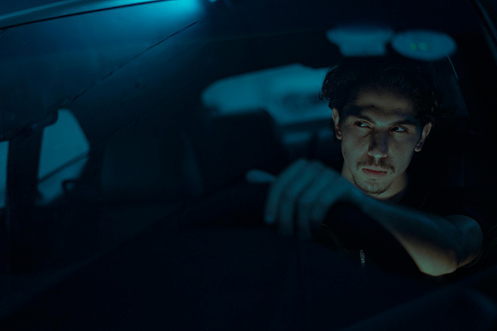 Man driving at night, looking serious, under dim blue lighting, representing a concept of leaving someone stranded.