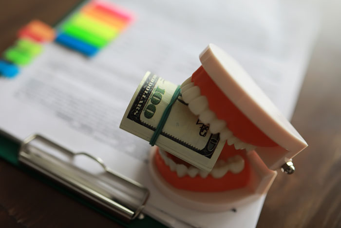 Dental insurance explained with toy teeth holding a hundred-dollar bill on a document.