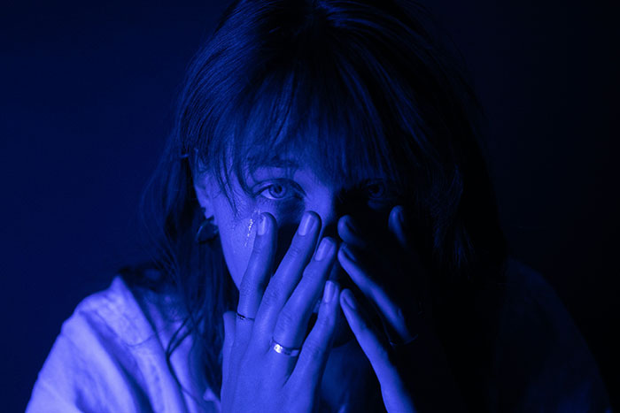 Woman in a blue-lit setting covering her face, reflecting on moving to a blue state for the first time.