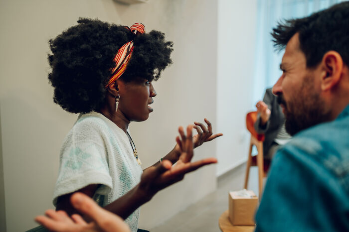 Two colleagues in a heated discussion, a woman gesturing with frustration and a man listening intently, emphasizing workplace conflict.