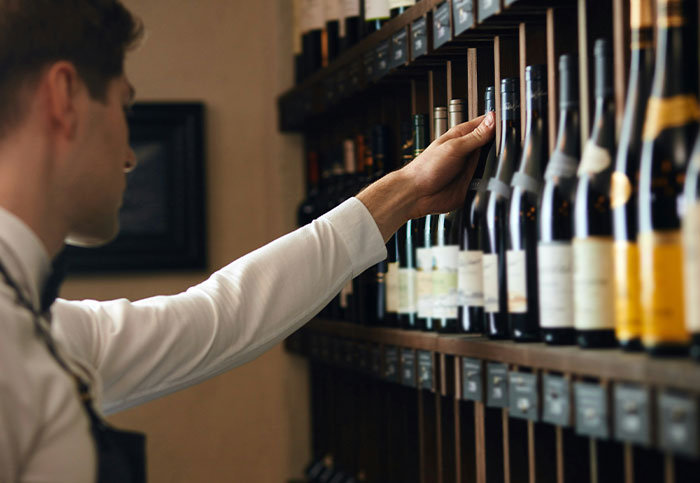 A customer browsing wine bottles on a shelf in a store, selecting one with careful consideration.