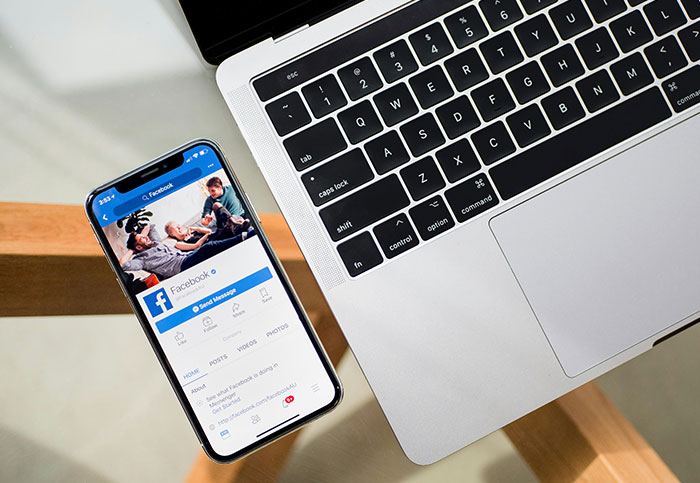Smartphone displaying Facebook app next to a laptop, symbolizing customer interactions online.