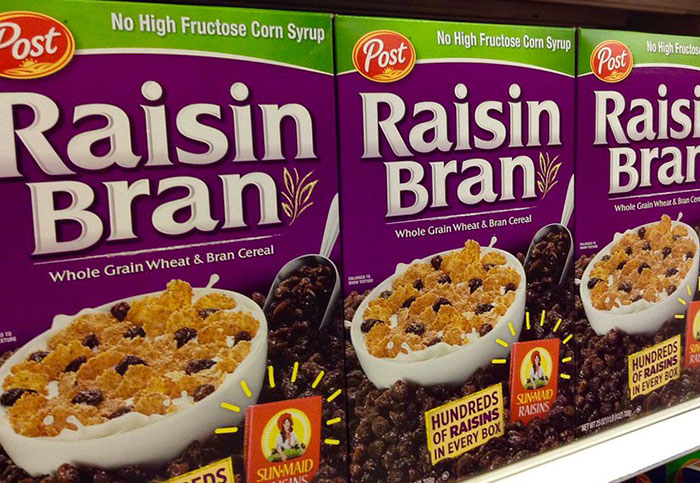 Raisin Bran cereal boxes on a store shelf, showcasing "hundreds of raisins in every box."