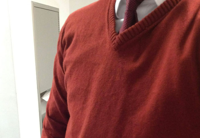A person in a red sweater and tie, standing by a gray cabinet, related to customer interactions and experiences.