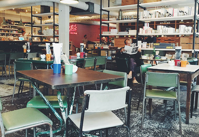 Cafe interior with people sitting, shelves filled with items, focusing on customer interactions.