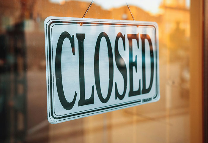 Closed sign hanging on a glass door, reflecting a street scene, illustrating a customer query situation.