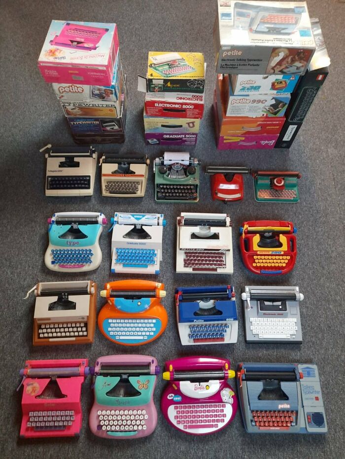 Collection of unique toy typewriters in various colors and designs, displayed on a gray surface.