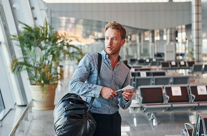 A man in a denim shirt at airport holding a ticket near empty seating area. A man in a denim shirt at airport holding a ticket near empty seating area.