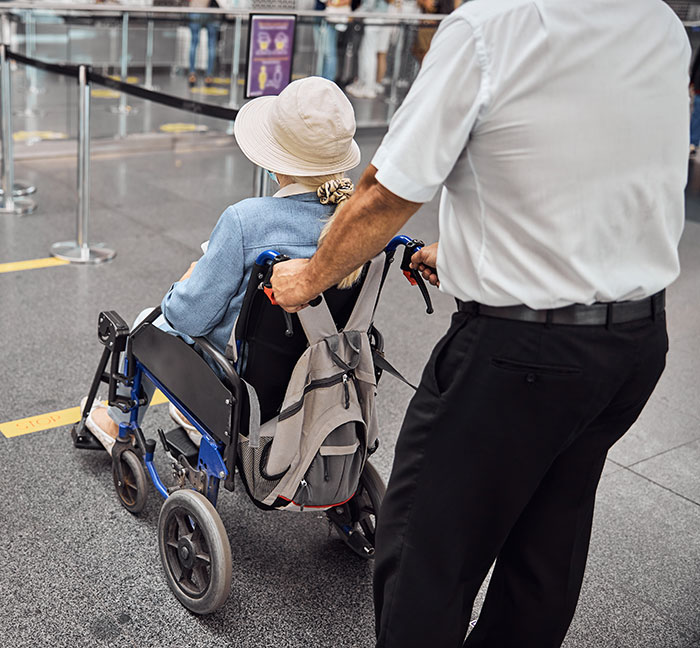 Man pushing woman in a wheelchair at airport, highlighting accessibility issues with passengers in wheelchairs. Man pushing woman in a wheelchair at airport, highlighting accessibility issues with passengers in wheelchairs.