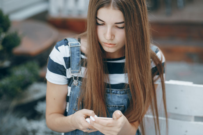 Young woman in overalls, checking her phone, looking pensive.