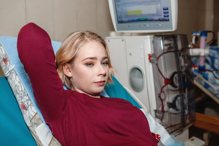 A woman in a hospital setting, reclining beside medical equipment, relating to an ex-friend's brother in care.