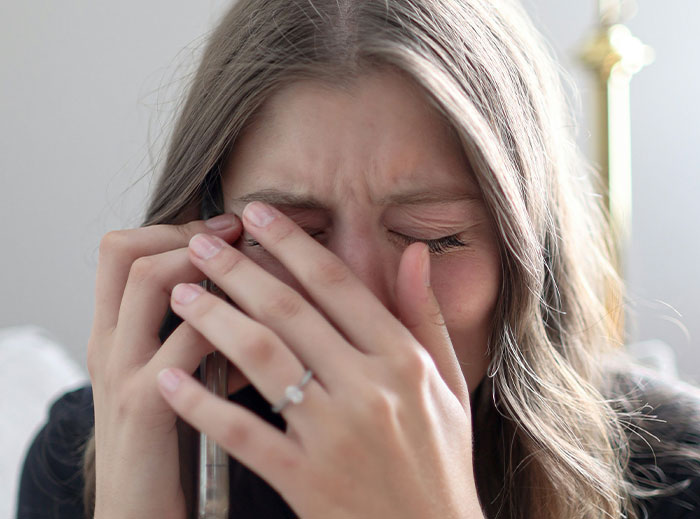 Distressed woman covering her face, holding a phone, highlighting emotional struggle.