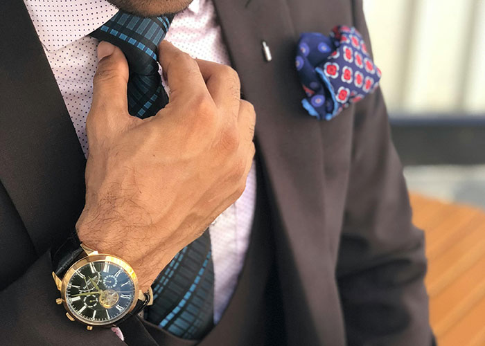 Person adjusting a tie, wearing a suit and watch, illustrating a CEO fail in professional attire.