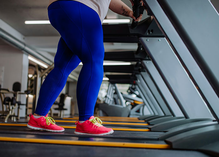 Person in blue leggings on a treadmill at the gym, highlighting fat-shaming issues and fitness. Person in blue leggings on a treadmill at the gym, highlighting fat-shaming issues and fitness.