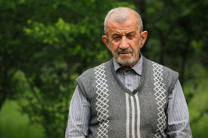 Elderly man outdoors in a patterned vest, representing a terrible father figure narrative.