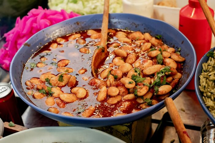 A large bowl of beans in sauce with wooden spoons, hinting at really messed up moments in cooking.