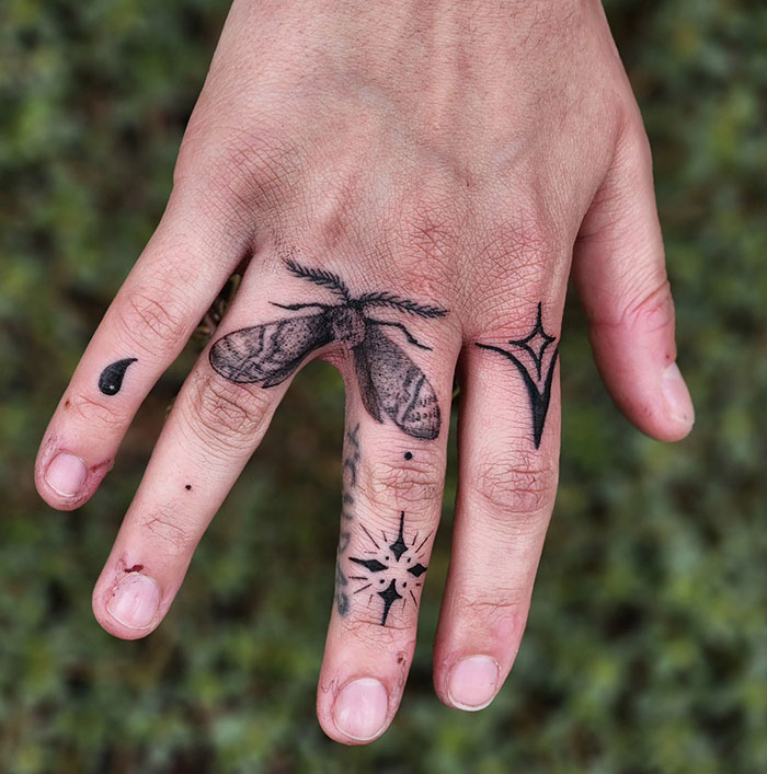 Hand with insect and geometric finger tattoos showcasing intricate designs.