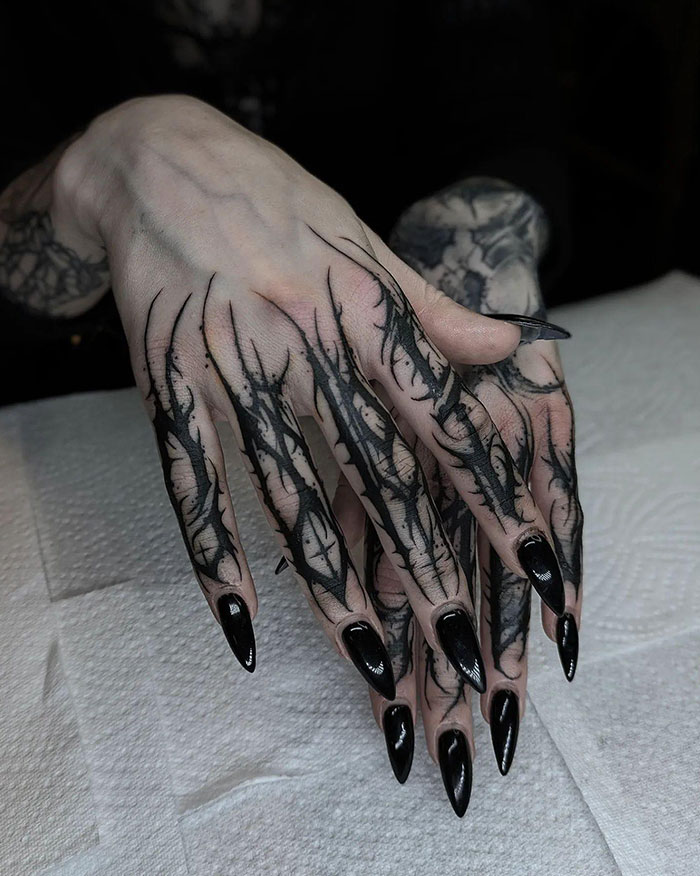 Intricate black finger tattoos on hands, showcasing artistic and detailed designs.