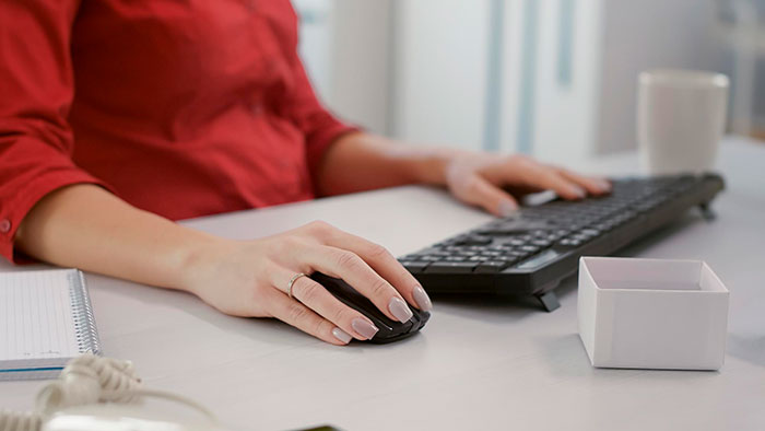 Person in a red shirt using a computer mouse at a tidy workspace, symbolizing unexpected work scenarios.
