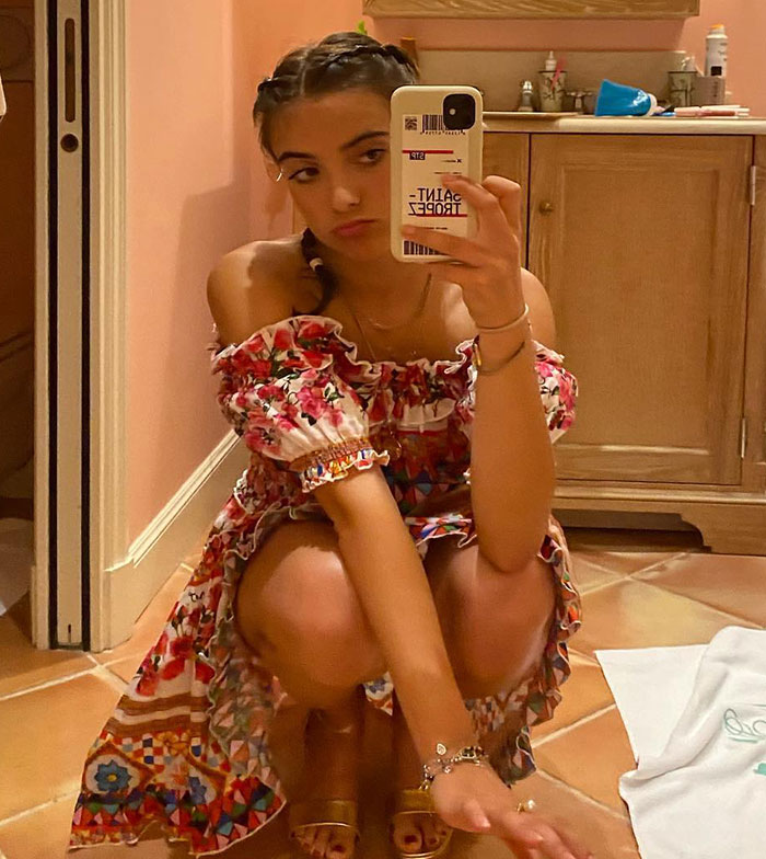 Young woman in floral dress taking a mirror selfie, related to viral "Mean Girl" antics and debutante discussions.