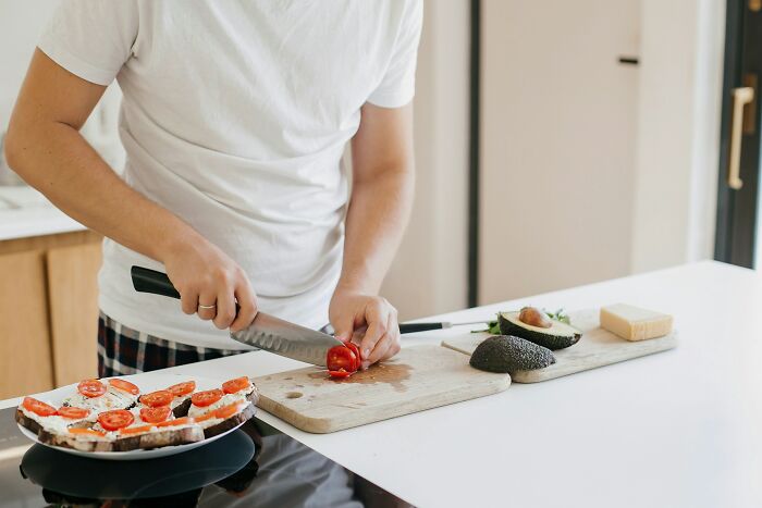Person chopping tomatoes on a cutting board, preparing a meal with avocados, reflecting a story of best friends turned strangers.