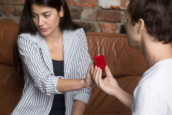 Man proposing with a ring, woman rejecting his proposal on a sofa.