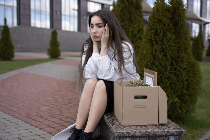 Woman sitting on a bench with a cardboard box, looking regretful after rejecting proposal.