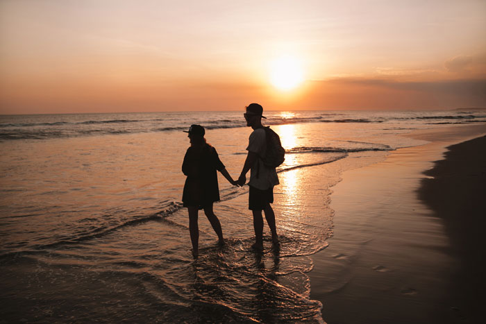Couple walking on the beach at sunset, holding hands.