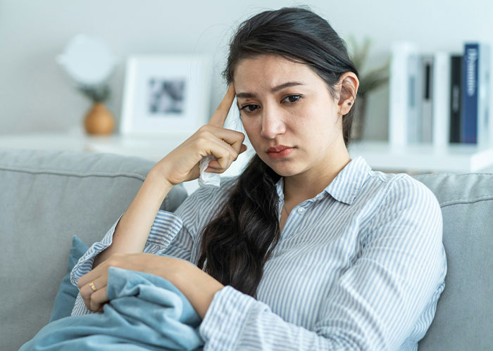 Woman looking upset while sitting on a couch, related to gift tag issue with MIL.