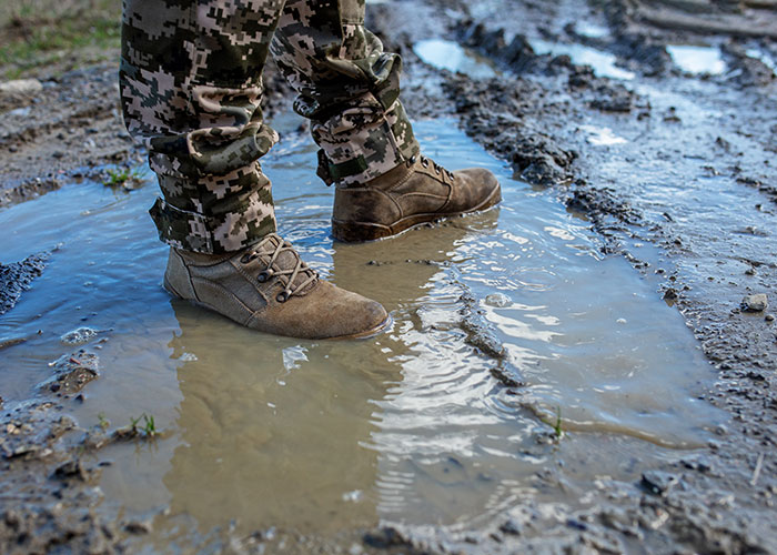 Camo pants and boots standing in a muddy puddle, representing water revenge.