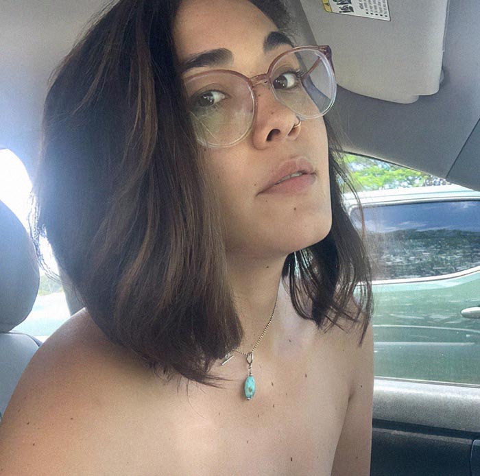 A woman with glasses and short hair sits in a car, wearing a gemstone necklace, focusing on her healing journey. A woman with glasses and short hair sits in a car, wearing a gemstone necklace, focusing on her healing journey.