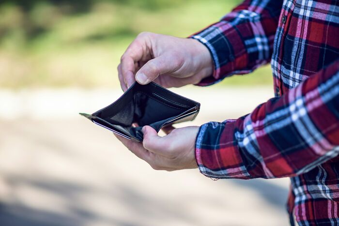 Person holding an empty wallet in an outdoor setting, wearing a plaid shirt, symbolizing relationship red flag professions.