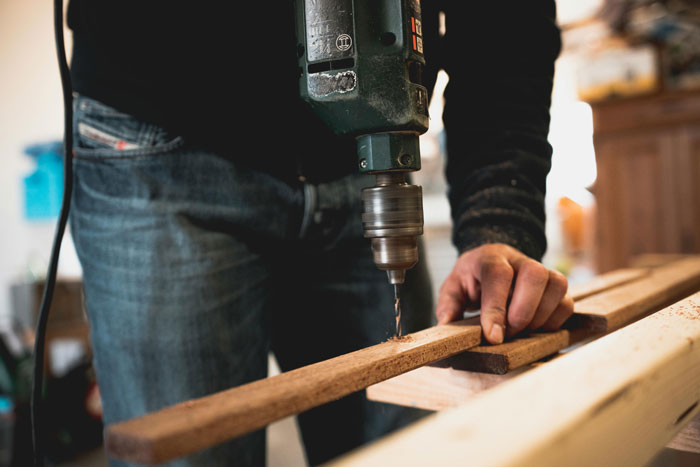 Person using a drill on wooden planks, working on an heirloom crib project.