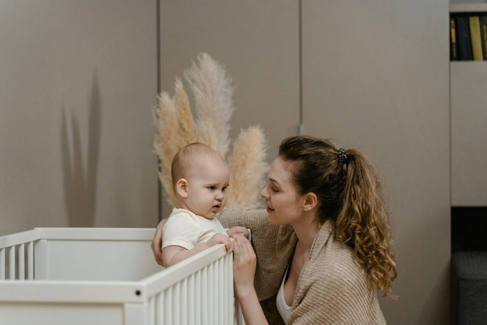 Woman with baby in a crib, thinking about raising her grandkid; parenting scene in a cozy room.