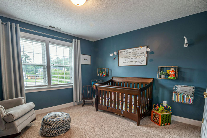 Heirloom crib in a cozy nursery with blue walls, next to a window and stuffed toys.
