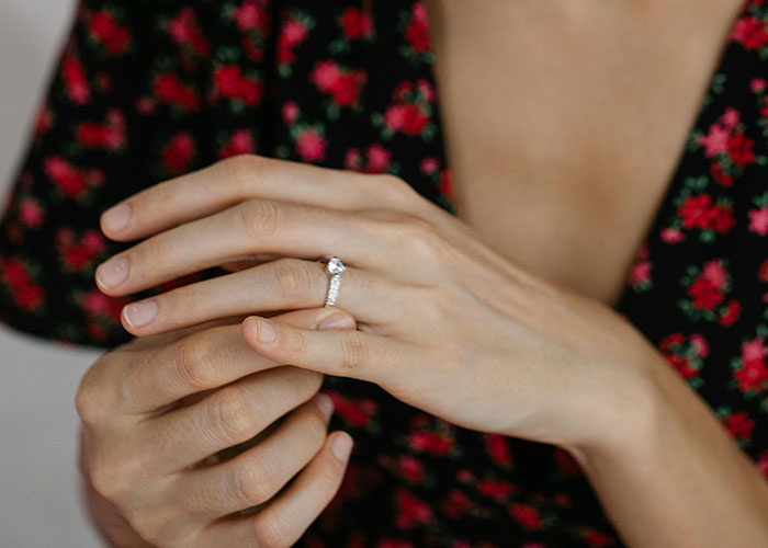 Woman adjusting ring on her finger, wearing a floral dress, symbolizing a revealing secret. Woman adjusting ring on her finger, wearing a floral dress, symbolizing a revealing secret.