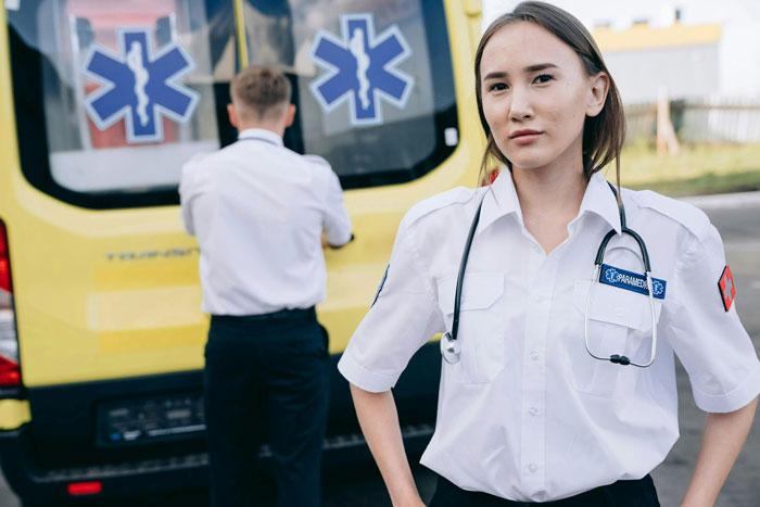 Paramedics in uniform standing near a yellow ambulance.