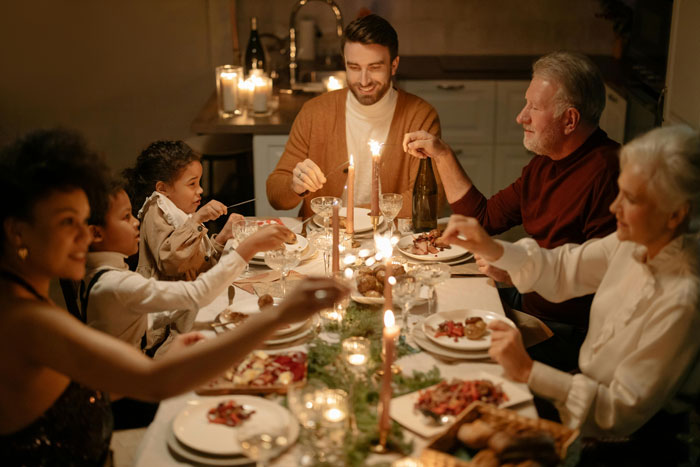 Family celebrating Christmas dinner around a table, enjoying a festive meal with candles and decorations.