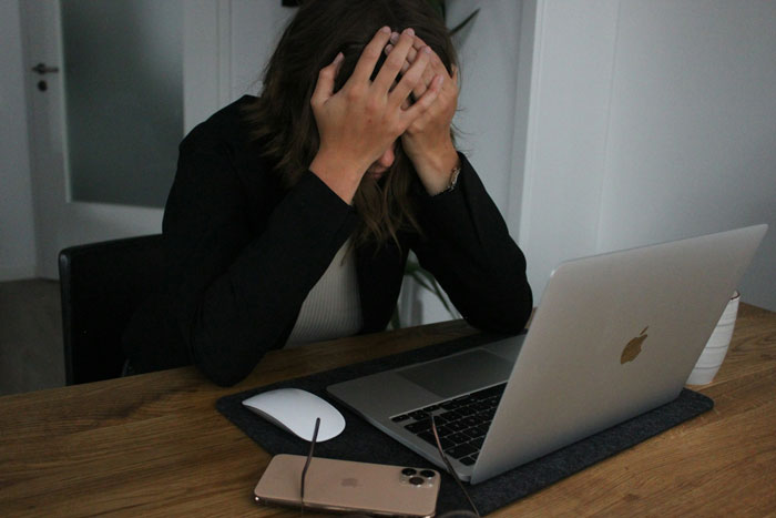 A frustrated woman at a desk with a laptop, holding her head during a critical job test.