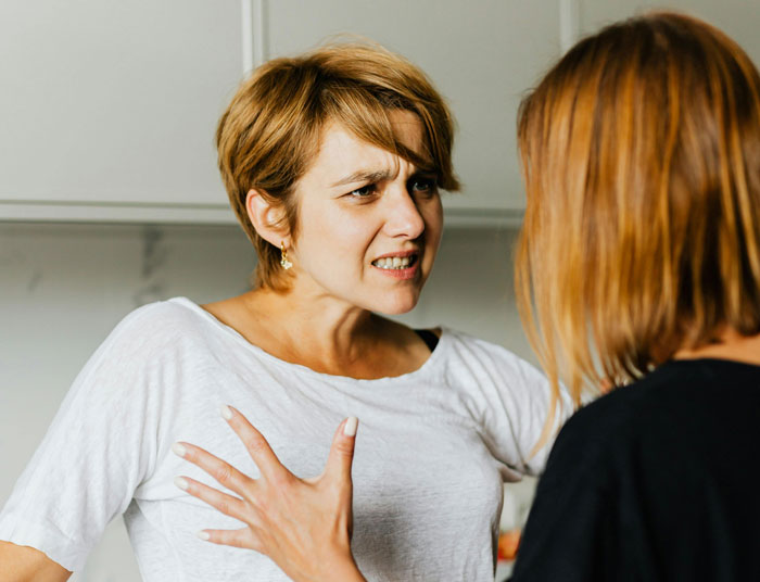 Woman argues over son-in-law's habit, gesturing angrily at another person in a heated discussion.