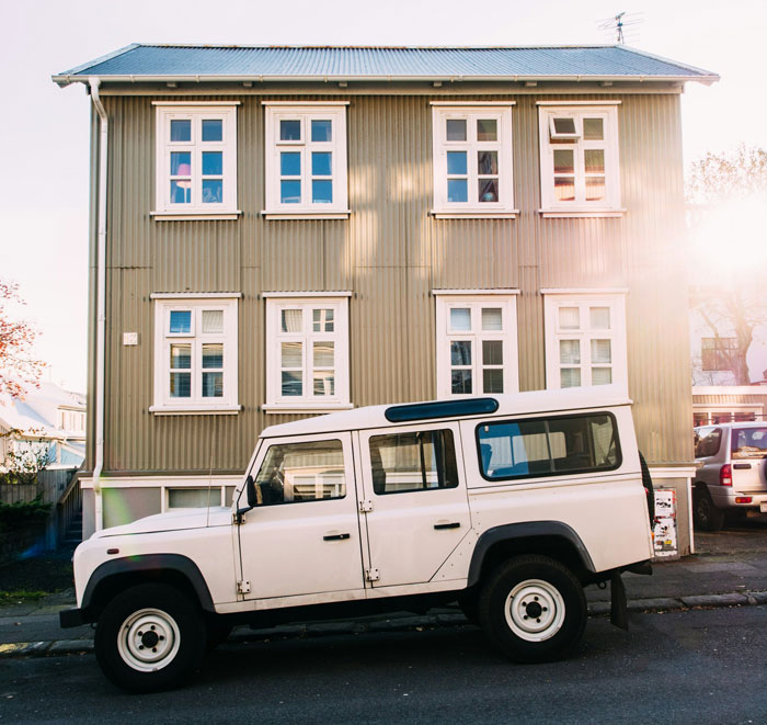 White SUV parked illegally near a residential building, sunlight gleaming on windows.