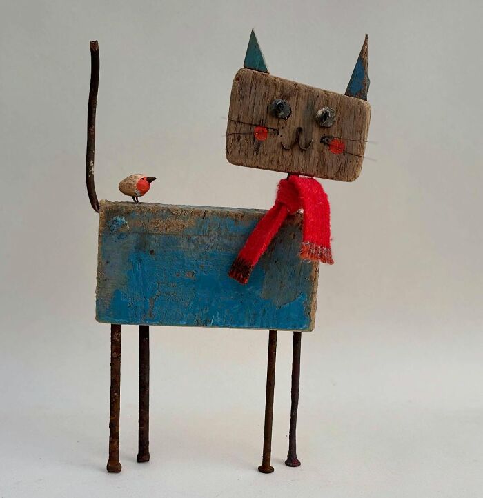 Driftwood animal sculpture of a cat with a red scarf and a small bird on its tail.