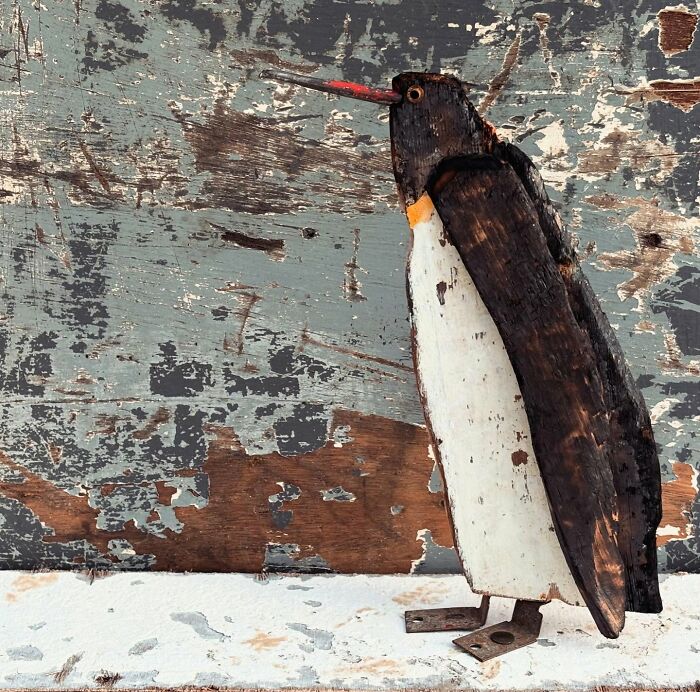 Driftwood animal sculpture of a penguin on a textured background.