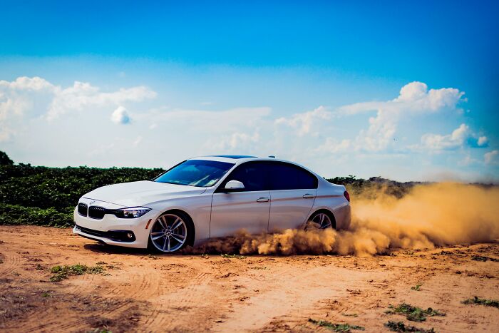 White BMW car drifting on a dirt road under a clear blue sky, illustrating industries built on illusions.